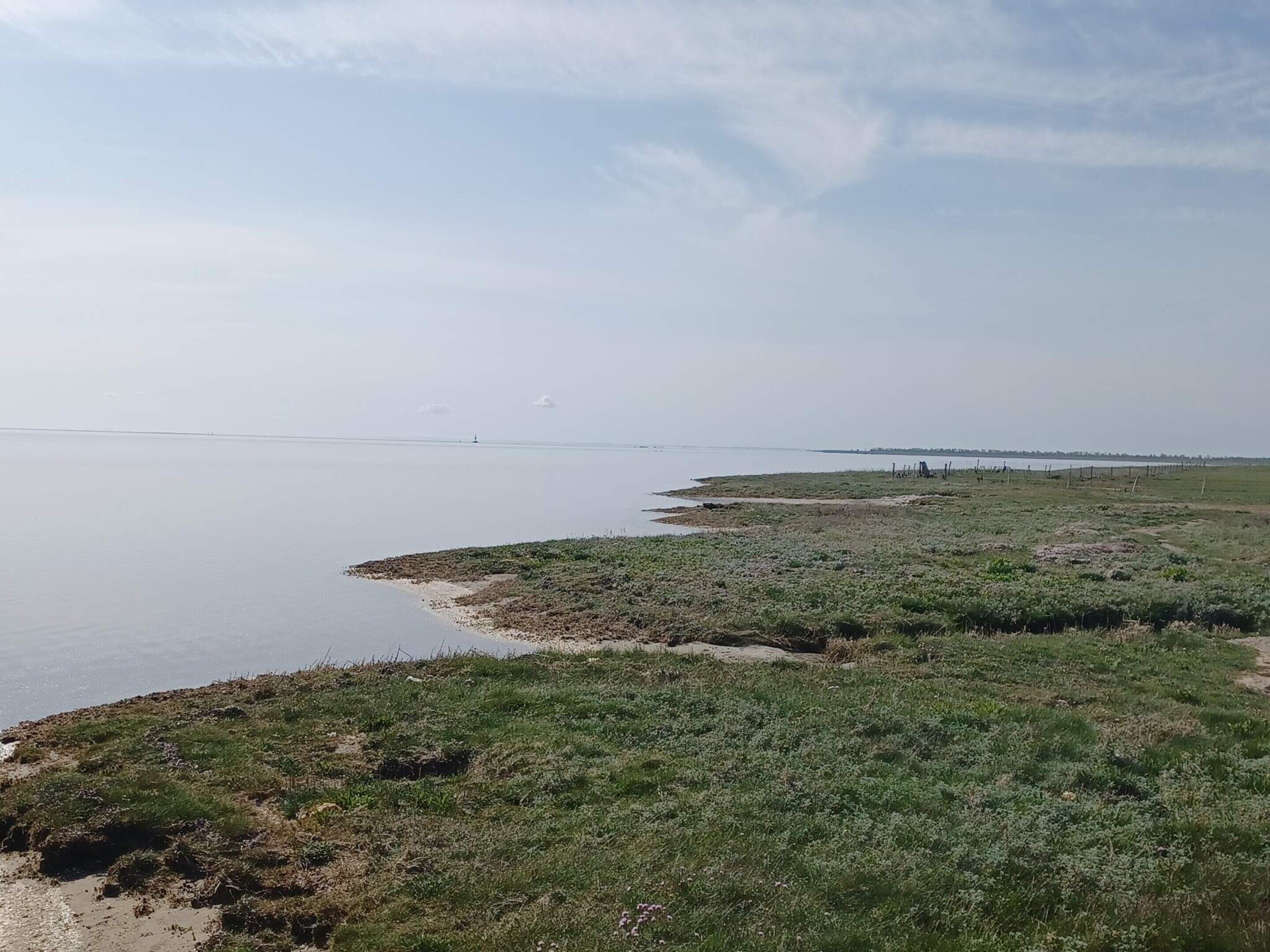 A coastal landscape with a sandy beach, grassy areas, and a distant view of a lighthouse.