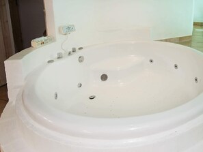 A white hot tub with multiple jets, a control panel, and a power outlet on the wall.