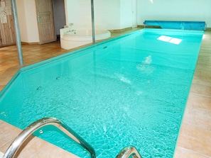 Une piscine à l’eau d’un bleu limpide, avec un escalier métallique et un banc bleu le long du bord.