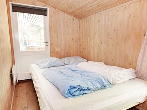 Habitación pequeña con cama individual, paredes de madera y puerta que da al exterior.