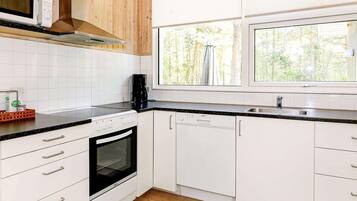 A kitchen with white cabinets, a black countertop, a microwave, a stove, a dishwasher, and a window with a view of trees.