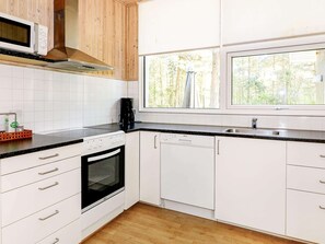 Een keuken met witte kasten, een zwart aanrecht, een magnetron, een fornuis, een vaatwasser en een raam met uitzicht op bomen.