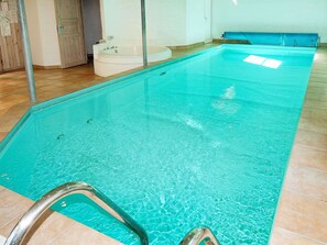 A swimming pool with a clear blue water surface, a metal pool ladder, and a blue bench along the side.