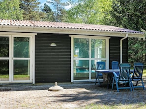 Ein kleines Gebäude mit einem Ziegeldach, großen Fenstern und einer Ziegelterrasse mit Außenbestuhlung.