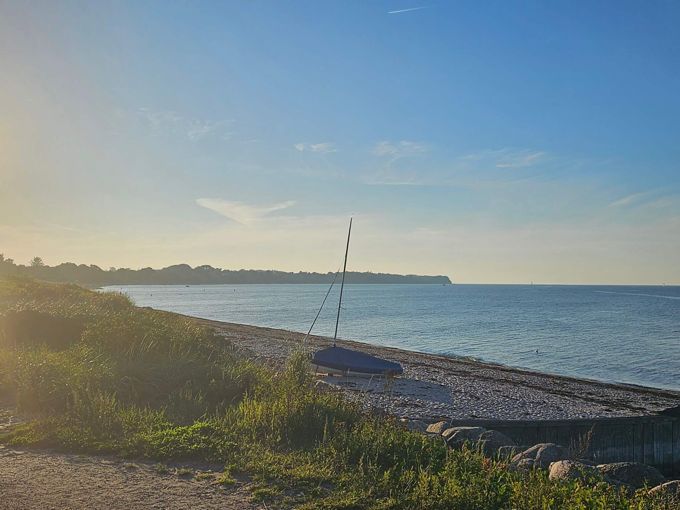 Ein Strand mit einem Segelboot, ruhigem Wasser und einer fernen Küstenlinie.