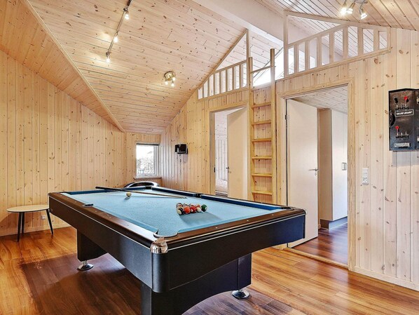 Une table de billard dans une pièce en bois, avec un plafond haut et une fenêtre.