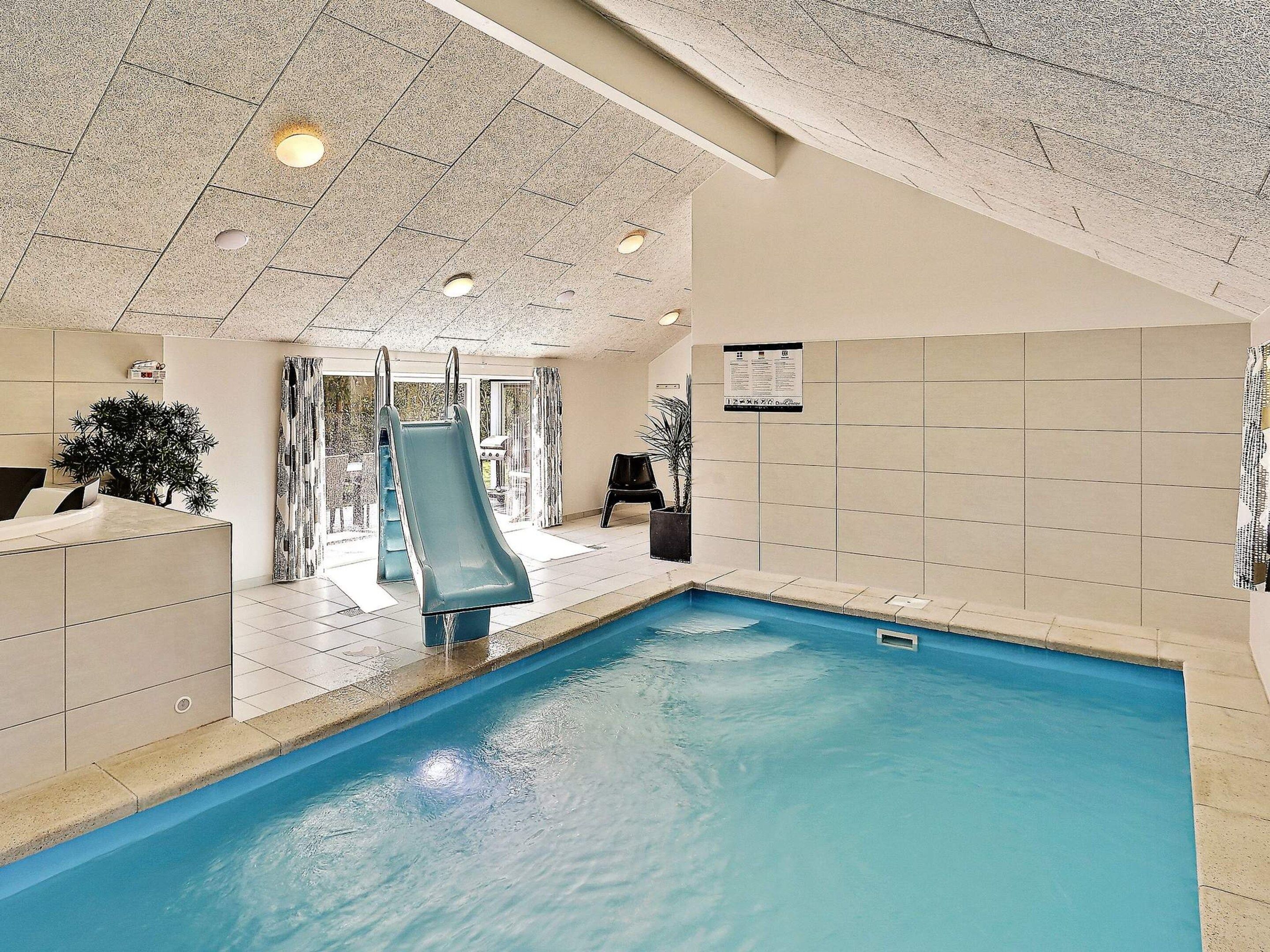 Une piscine intérieure avec un toboggan, des murs carrelés et un plafond doté d’un éclairage encastré.