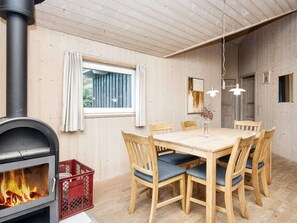 A dining area with a wooden table and chairs, a fireplace, and a window with curtains. - 6 Person Holiday Home in Harboore (Harboore)