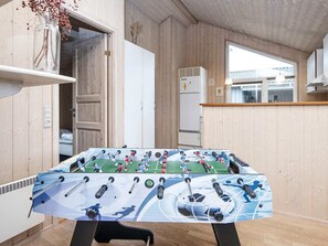 Una habitación con mesa de fútbol, paredes de madera, una puerta blanca y una ventana.