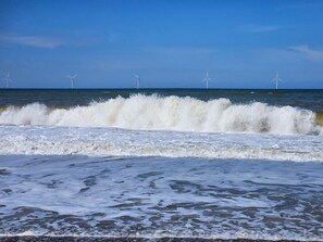 A beach with waves and wind turbines in the distance.