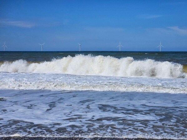 A beach with waves and wind turbines in the distance.
