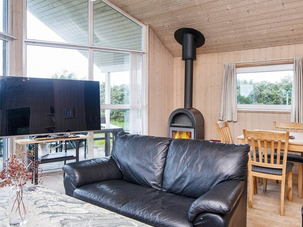 Una sala moderna con un sofá de cuero, televisor, chimenea y comedor con muebles de madera.