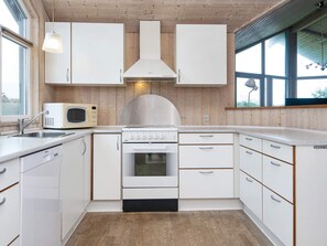 A modern kitchen with white cabinets, a microwave, a stove, and a large window providing natural light. - 6 Person Holiday Home in Harboore (Harboore)
