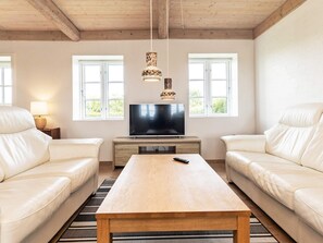 Un salon avec un téléviseur, deux canapés en cuir blanc, une table basse en bois et un tapis à motifs.
