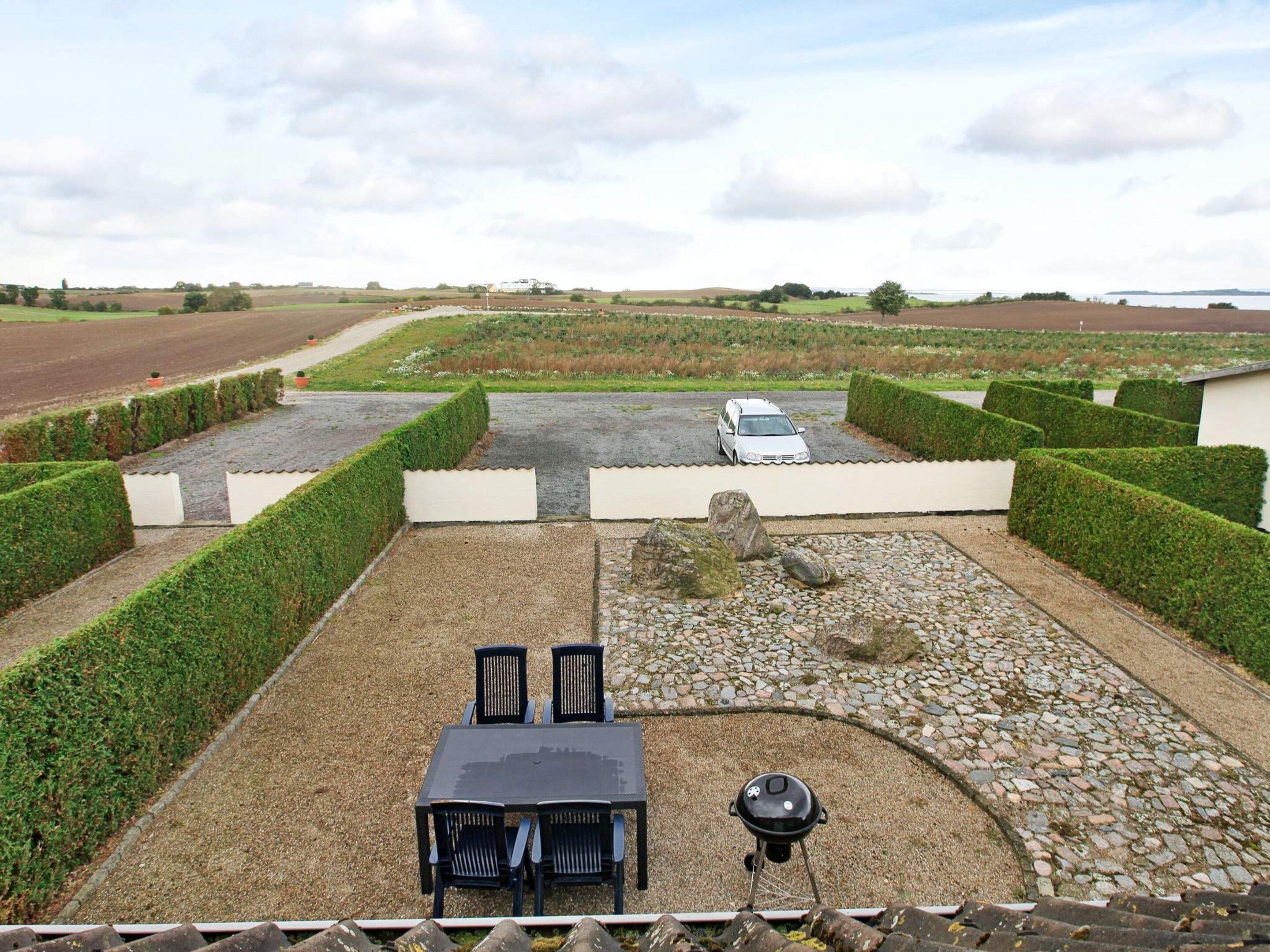 A patio with a table and chairs, a barbecue grill, and a car parked in the background.