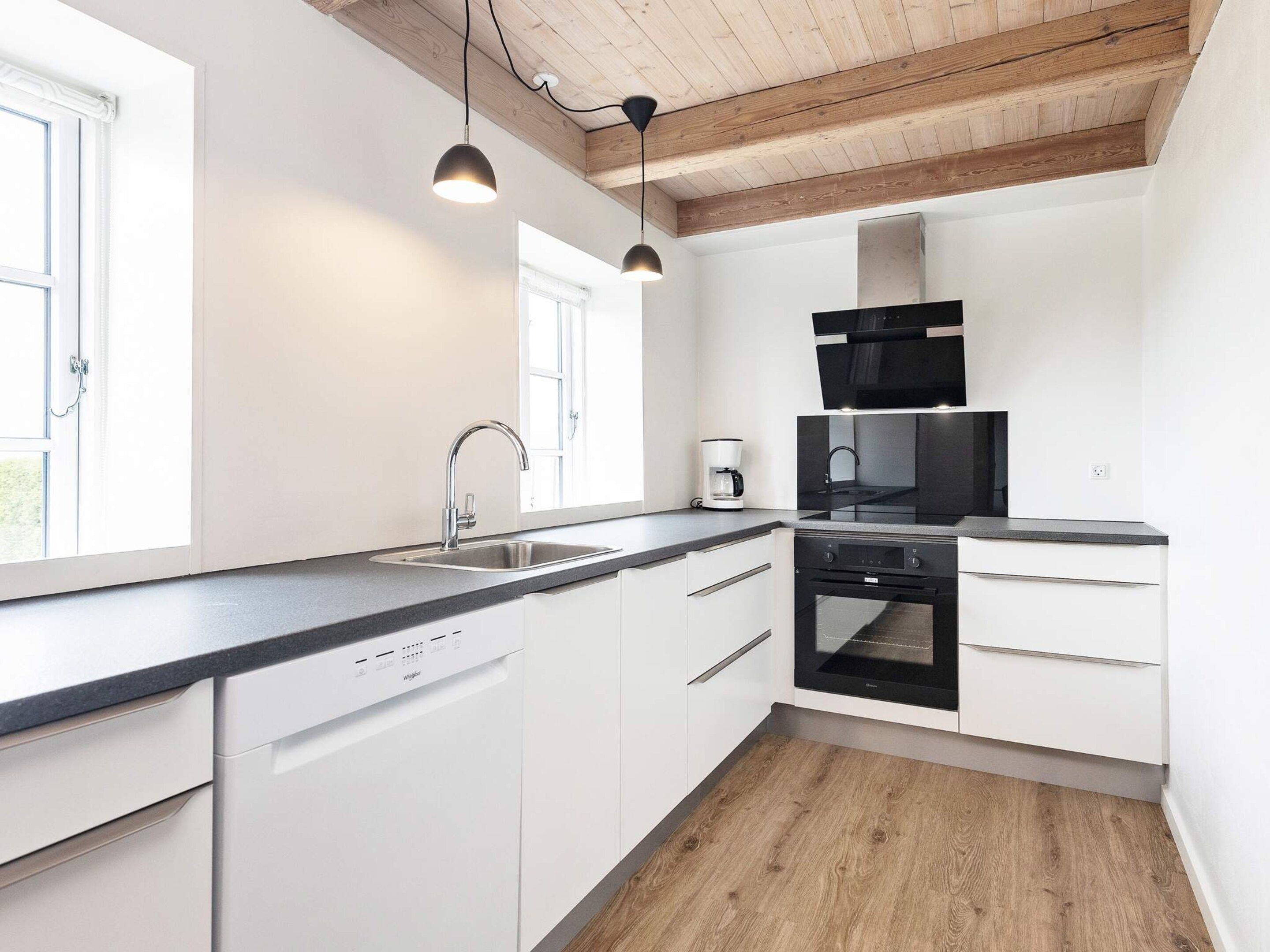 A modern kitchen with white cabinetry, a black stove, and a wooden ceiling.