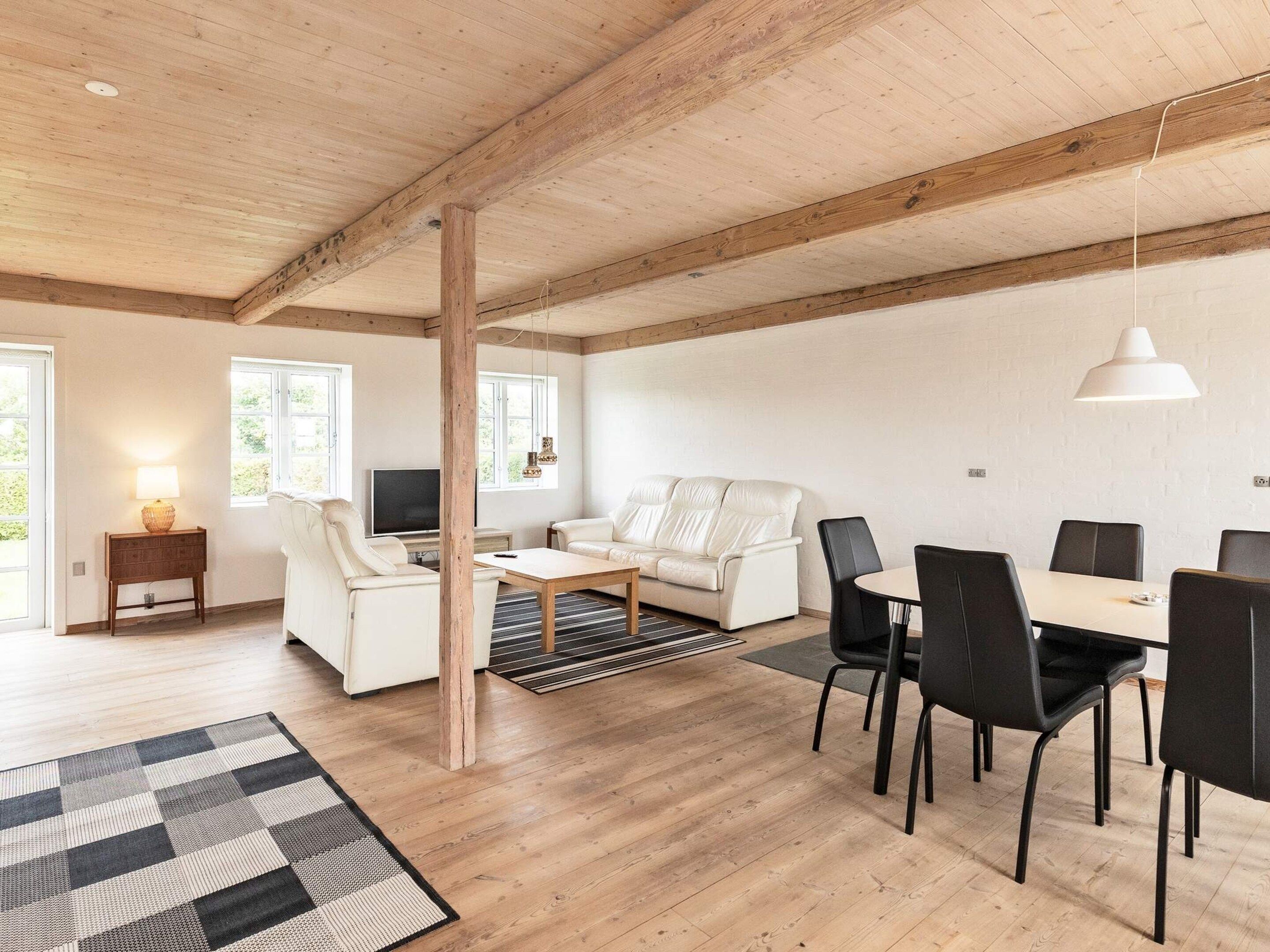 A spacious living area with a wooden ceiling, a white sofa, a dining table with chairs, and a television.