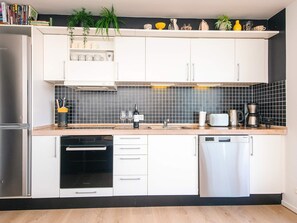 A modern kitchen with white cabinets, a black tiled backsplash, a stainless steel refrigerator, a dishwasher, and a coffee maker. - 4 Star Holiday Home in Hejls (Hejls)