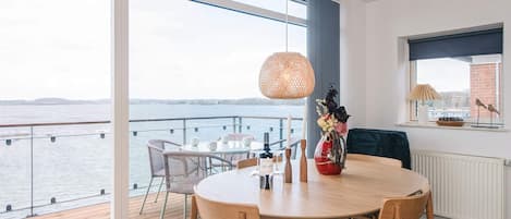Un espace de repas moderne avec une table et des chaises en bois, un vase rempli de fleurs et une vue sur l’eau.