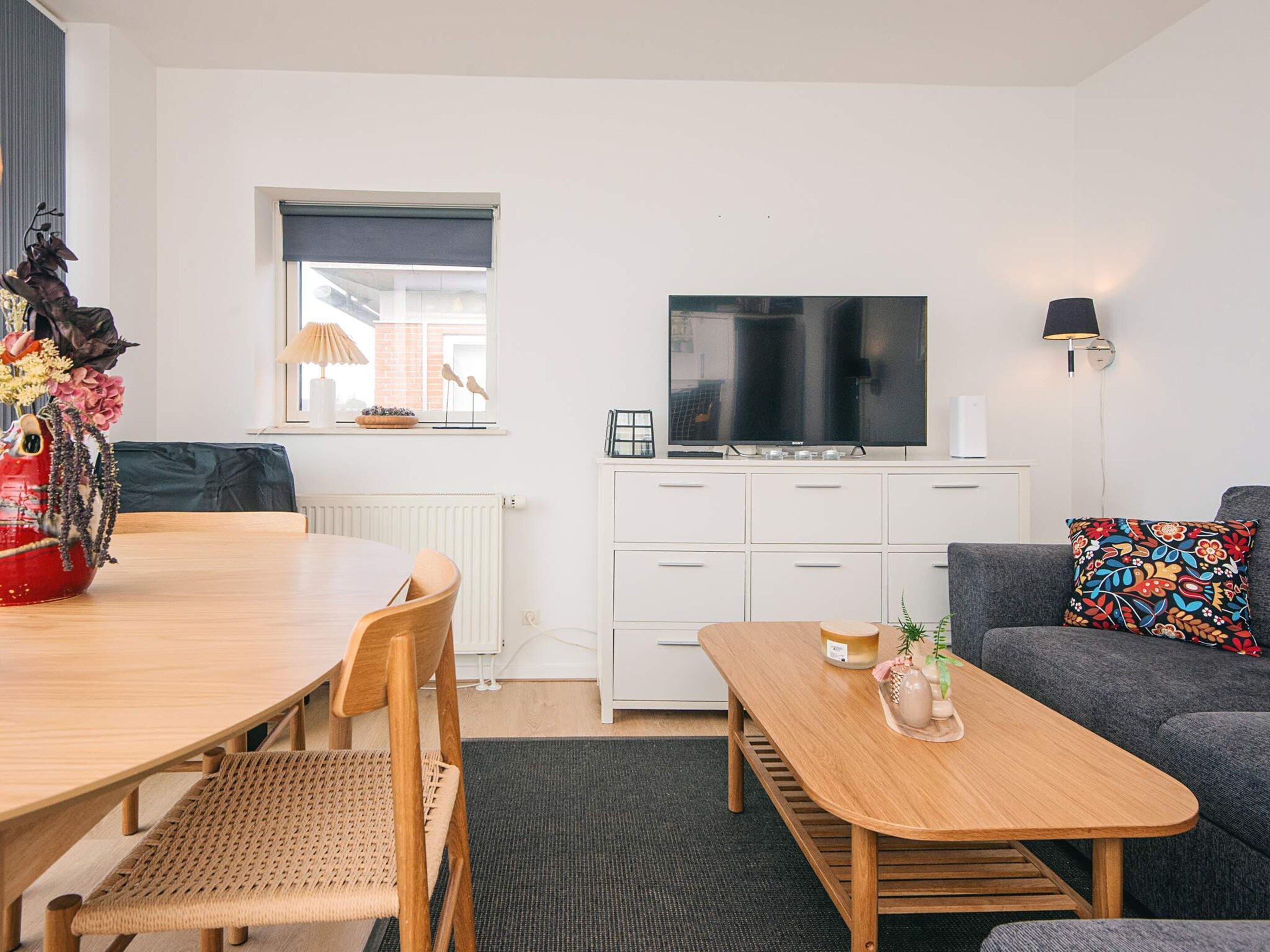 Una sala moderna con comedor, sofá, televisor y ventana con persianas.