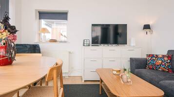 Una sala moderna con comedor, sofá, televisor y ventana con persianas.