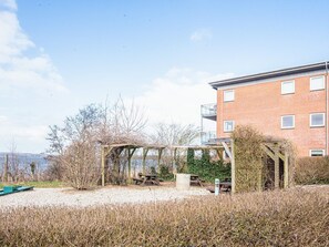 A building with a brick facade, a wooden pergola, and a gravel area with picnic tables. - 4 Star Holiday Home in Hejls (Hejls)