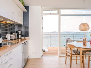 A modern kitchen with a view of the sea, a dining area with wooden furniture, and a balcony with a railing. - 4 Star Holiday Home in Hejls (Hejls)
