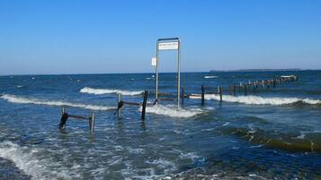 Escena costera con un cartel en el agua, olas y un muelle de madera.