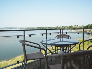 A balcony with wicker chairs and a glass table overlooking a calm body of water with boats.