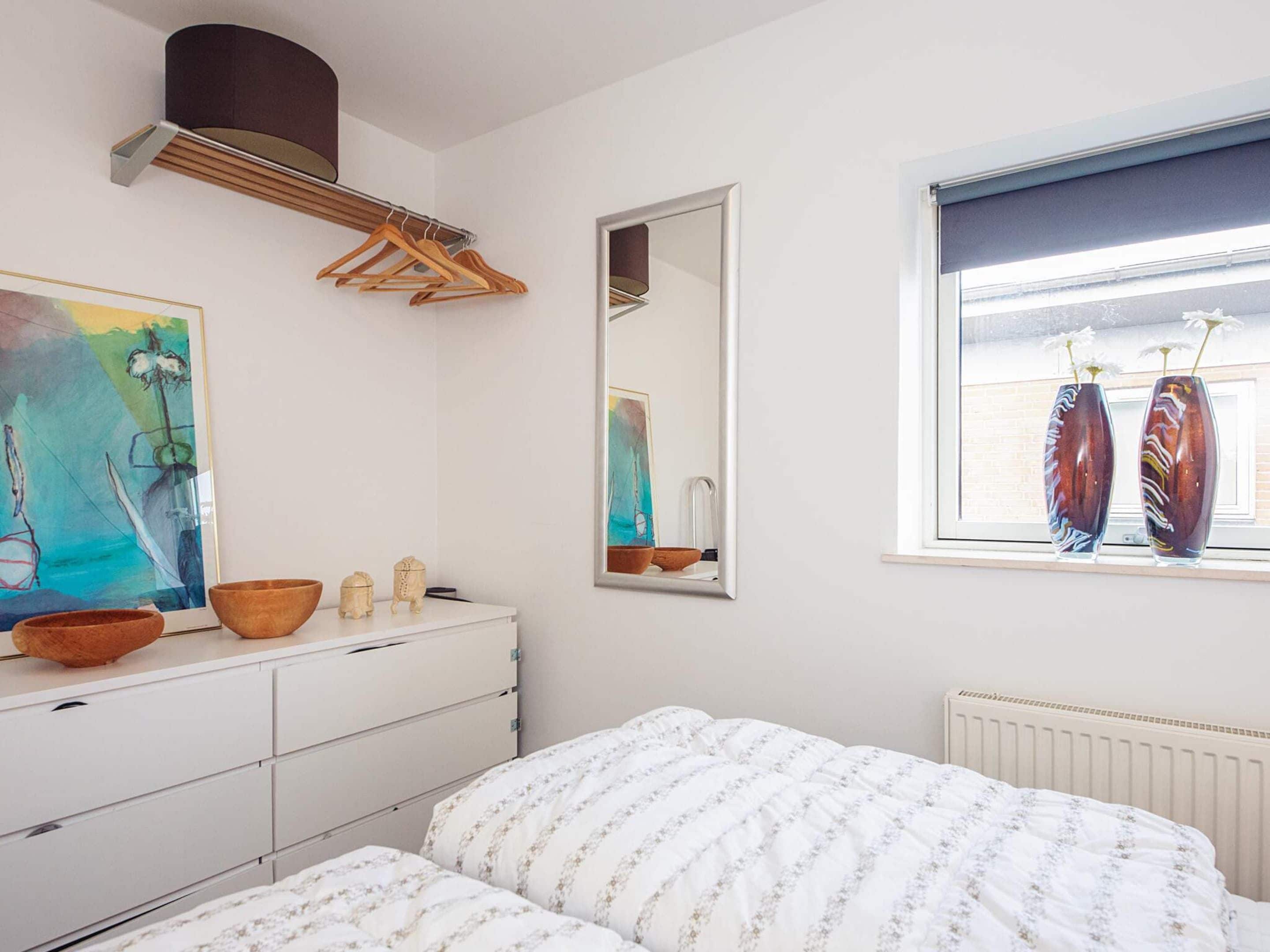 A bedroom with a bed, dresser, mirror, and window with decorative vases.