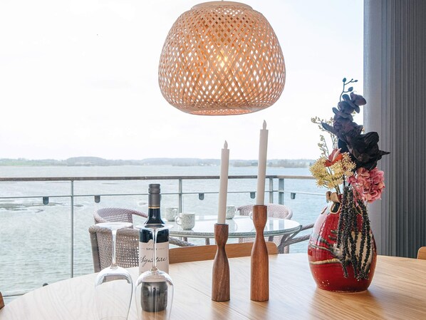 A table with a bottle, candles, and a vase with flowers by a window overlooking a body of water. - 4 Star Holiday Home in Hejls (Hejls)