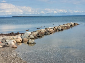 Une côte rocheuse bordée d’une mer calme, avec une étendue terrestre visible au loin.