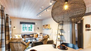 A cozy living room with a wooden ceiling, a round table with fruit and tea, and a large hanging light fixture. - Holiday Home in FÃ¥vang (Ringebu)