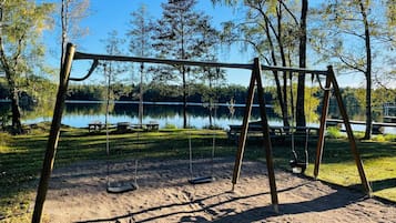 A park with a swing set and picnic tables by a lake.