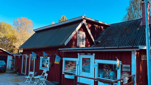 A red building with a blue door and windows, a sign reading "Ingång" and "Entré", and a small outdoor seating area with white chairs. - 4 Person Holiday Home in Hallabro (Hallaröd)
