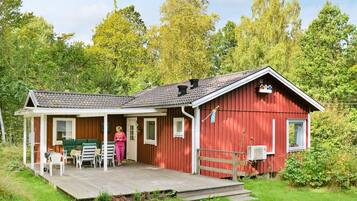 A red cabin with a porch, a covered outdoor seating area, and a small deck.