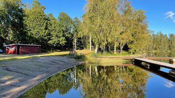 A tranquil lakeside setting with a dock, a small red building, and dense trees reflecting in the calm water.