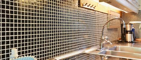 A kitchen with a black tiled backsplash, stainless steel sink, and a coffee machine.