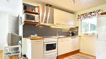 A modern kitchen with white cabinetry, a microwave, an oven, and a stove. There is a window with a view of greenery outside.