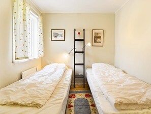 A room with two single beds, a radiator, a window with curtains, a lamp, and two framed pictures on the wall. - 4 Person Holiday Home in Hallabro (Hallaröd)