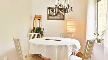 A dining room with a round table, white chairs, a chandelier, a painting, and a floor lamp.
