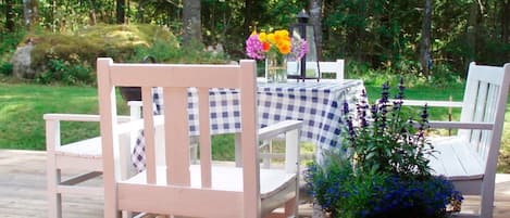 A wooden deck with a checkered tablecloth, white chairs, and a potted plant.