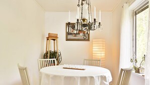 A dining room with a round table, white chairs, a chandelier, a painting, and a floor lamp. - 4 Person Holiday Home in Hallabro (Hallaröd)