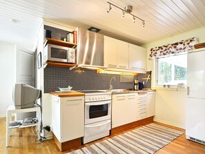 A modern kitchen with white cabinetry, a microwave, an oven, and a stove. There is a window with a view of greenery outside. - 4 Person Holiday Home in Hallabro (Hallaröd)