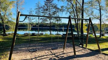 A swing set in a park with picnic tables and a lake in the background.