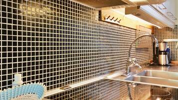 A kitchen with a black tiled backsplash, stainless steel sink, and a range hood.