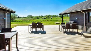 A wooden deck with outdoor furniture, including tables and chairs, overlooking a grassy field. - 5 Star Holiday Home in Vejby (Vejby)