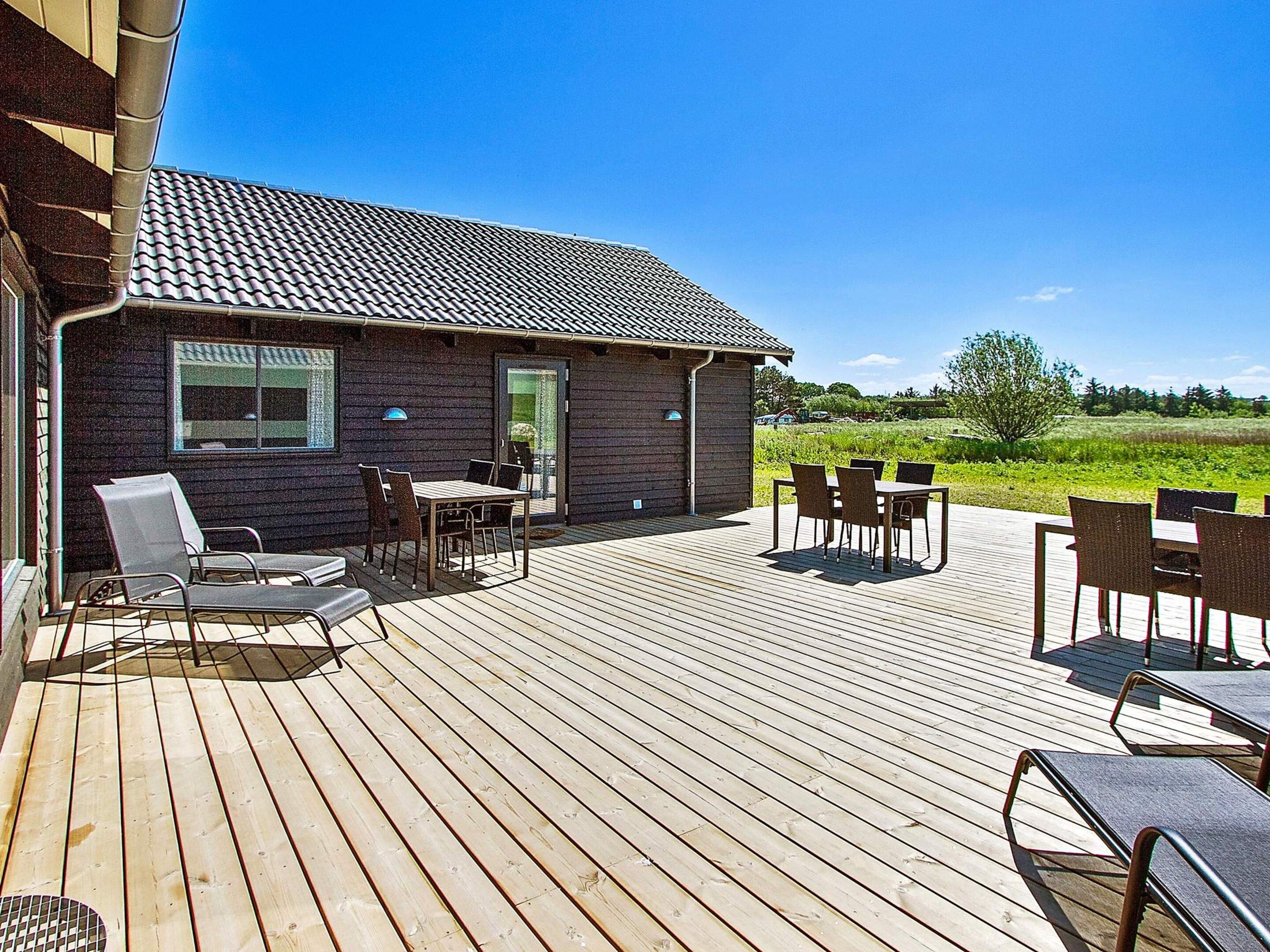 A wooden deck with outdoor furniture, a building with a tiled roof, and a grassy field in the background.