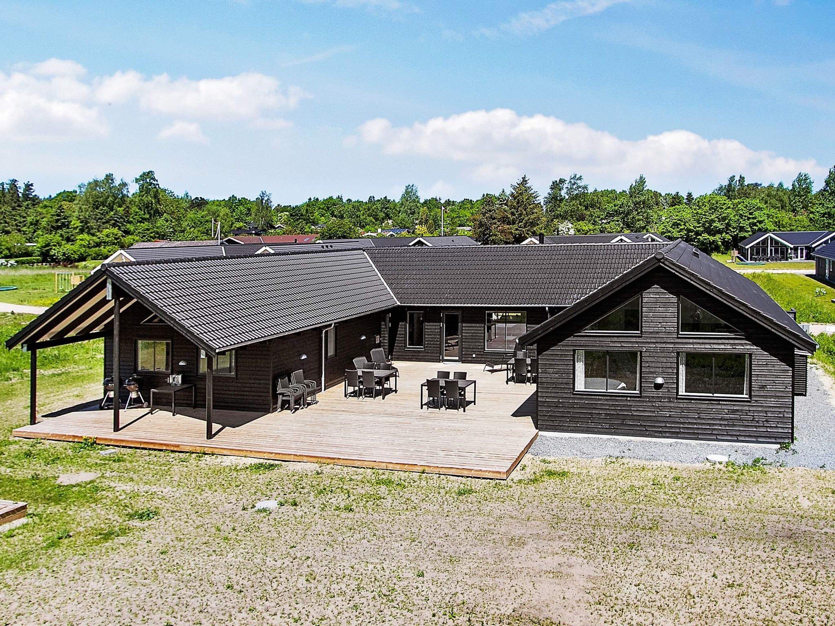 A modern building with a large deck area, multiple windows, and a covered outdoor seating area.