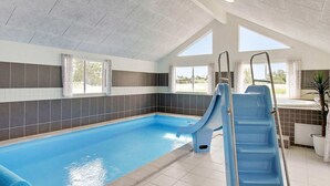 An indoor swimming pool with two slides, a ladder, and a view of the outdoors through large windows. - 5 Star Holiday Home in Vejby (Vejby)